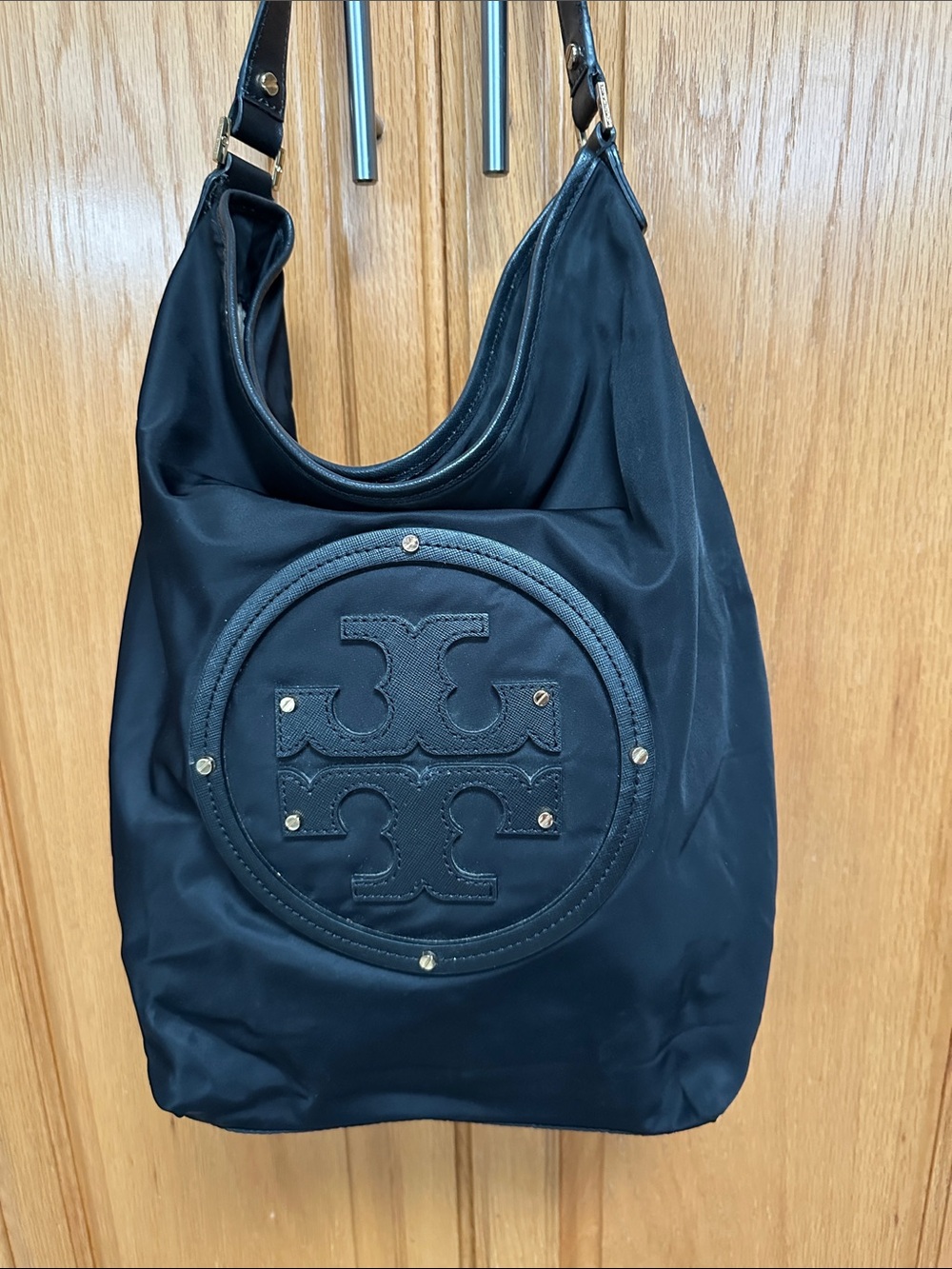 Tory Burch vinyl hobo bag with gold rivets on large emblem. Tan interior.